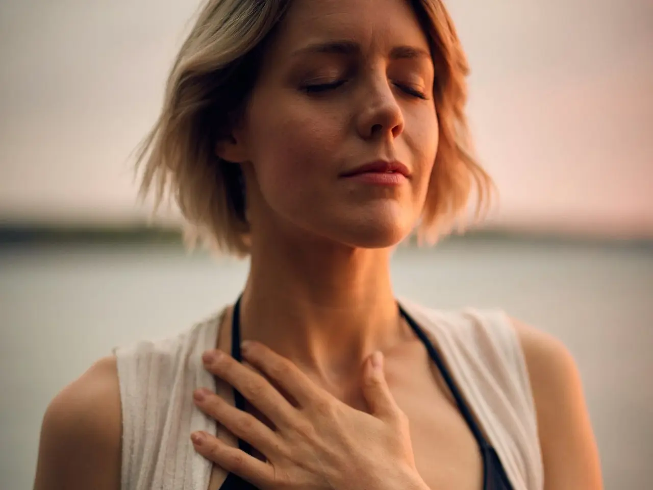 woman in white vest and black bikini with hand on chest